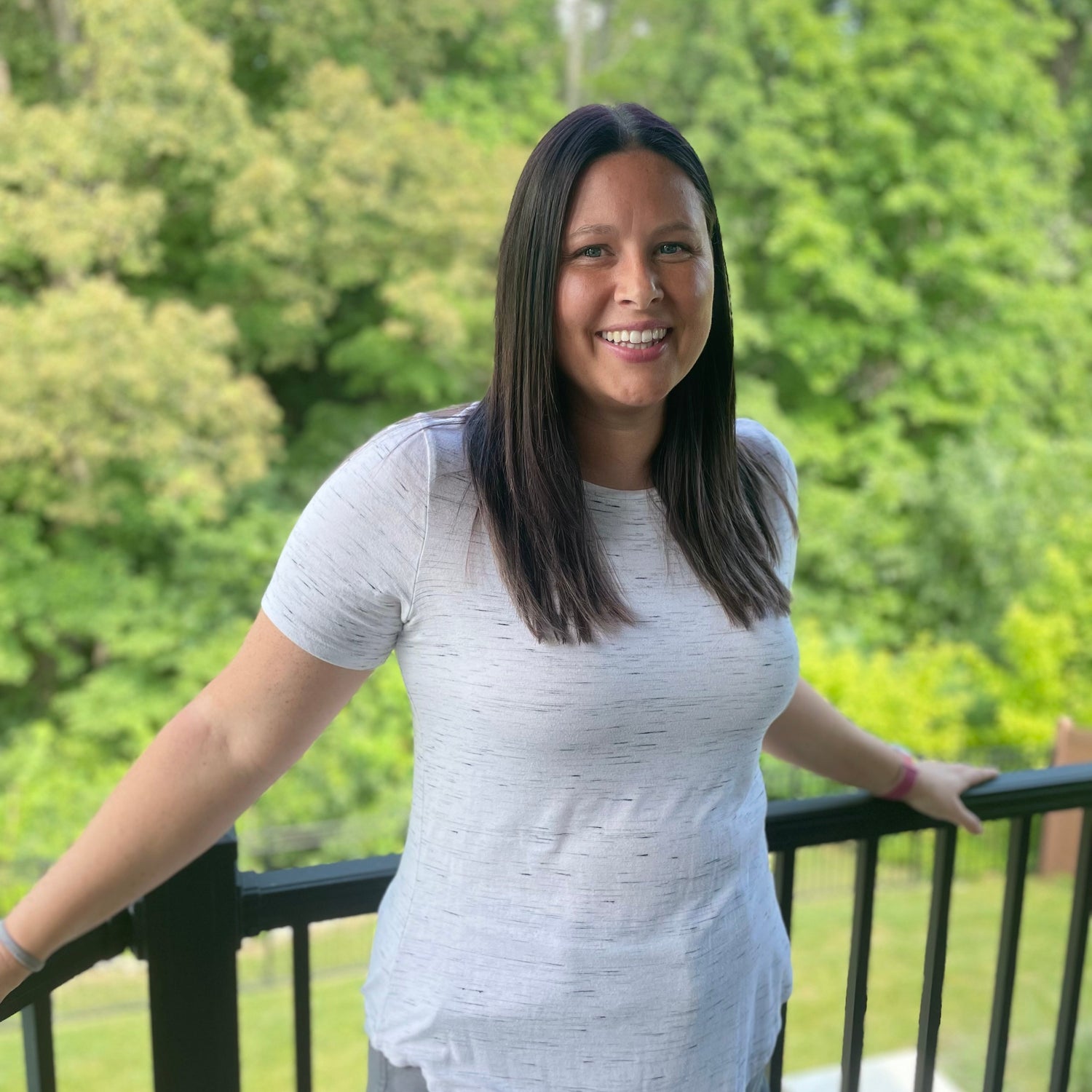 Woman standing on a balcony with green trees in the background