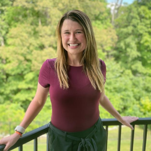 Woman standing on a balcony with greenery in the background